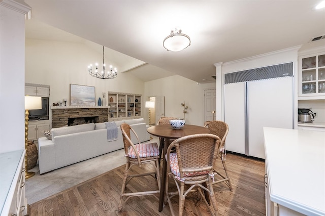 dining room featuring hardwood / wood-style flooring, a notable chandelier, a stone fireplace, and vaulted ceiling