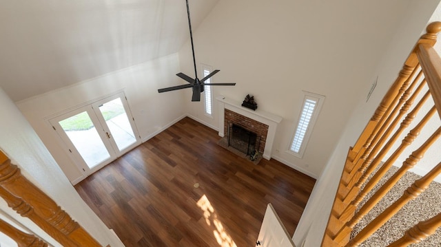 unfurnished living room with french doors, a brick fireplace, a towering ceiling, ceiling fan, and dark wood-type flooring