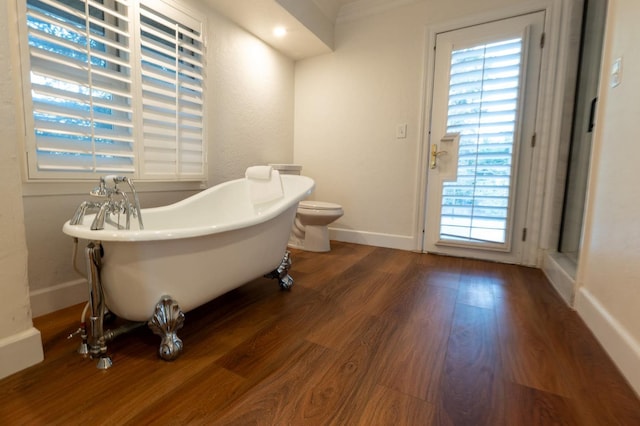 bathroom with toilet, a tub to relax in, and hardwood / wood-style floors