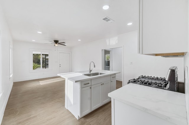 kitchen with a kitchen island with sink, white cabinets, sink, light hardwood / wood-style floors, and range