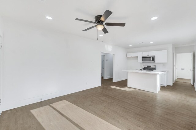 kitchen with a center island with sink, ceiling fan, appliances with stainless steel finishes, dark hardwood / wood-style flooring, and white cabinetry