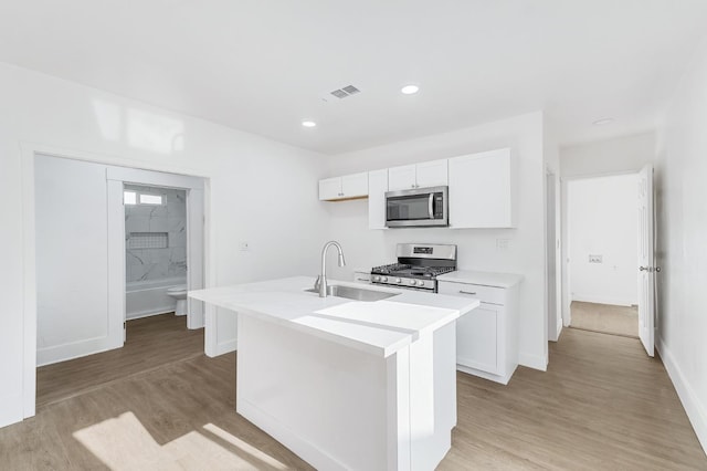 kitchen with light wood-type flooring, stainless steel appliances, white cabinetry, and a center island with sink