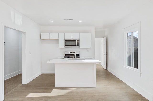 kitchen with white cabinetry, sink, stainless steel appliances, light hardwood / wood-style floors, and a kitchen island with sink