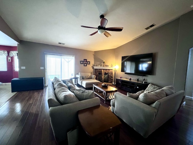 living room with dark hardwood / wood-style floors, ceiling fan, and a stone fireplace