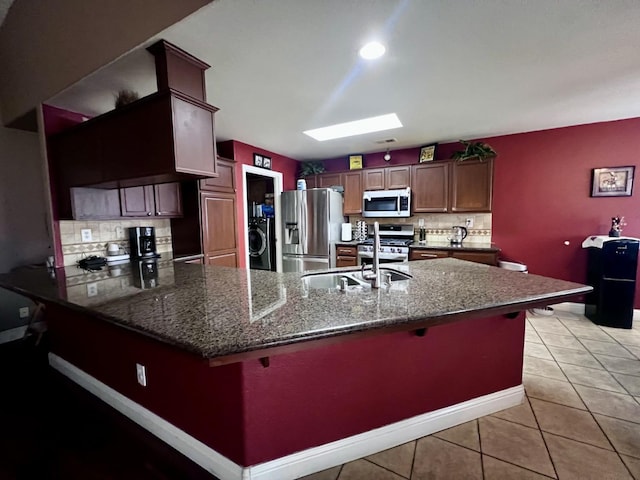 kitchen with sink, stainless steel appliances, backsplash, washer / clothes dryer, and a breakfast bar