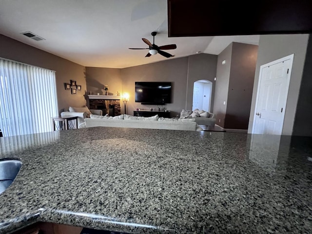 kitchen with a fireplace, vaulted ceiling, ceiling fan, and stone counters