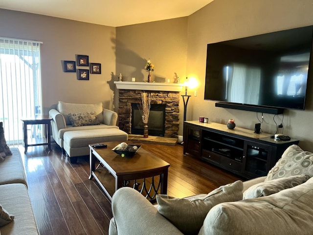 living room featuring a stone fireplace and dark wood-type flooring