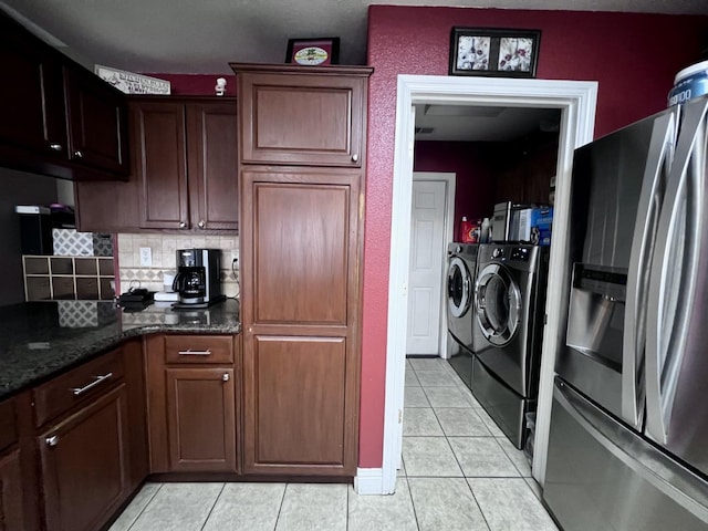 kitchen featuring backsplash, dark stone countertops, stainless steel fridge, washer and clothes dryer, and light tile patterned floors