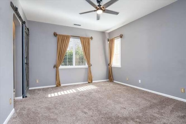 empty room with ceiling fan, a barn door, and carpet