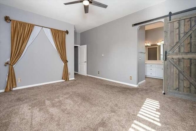 unfurnished bedroom with connected bathroom, carpet floors, a barn door, and ceiling fan