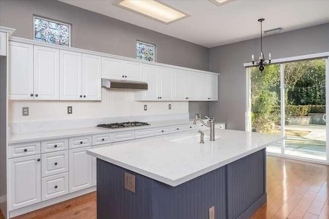 kitchen with sink, white cabinetry, hanging light fixtures, stainless steel gas stovetop, and a kitchen island with sink