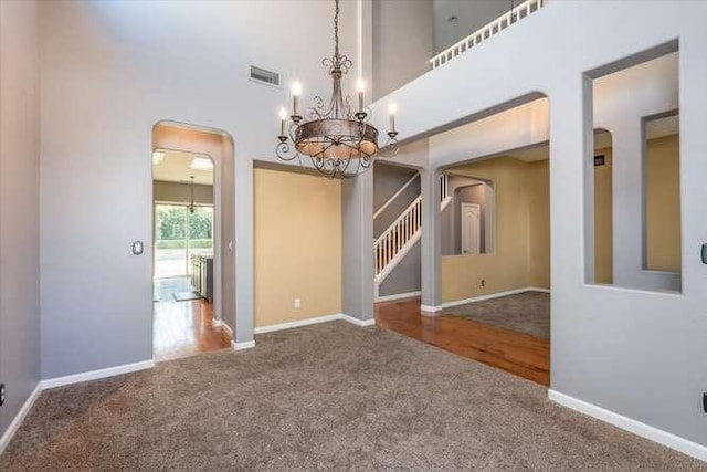 carpeted empty room with an inviting chandelier and a high ceiling