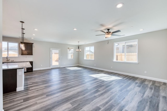 unfurnished living room with ceiling fan with notable chandelier, dark wood-type flooring, and sink