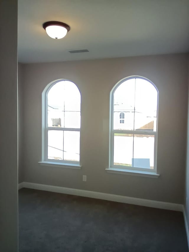 unfurnished room with a wealth of natural light, baseboards, and dark colored carpet