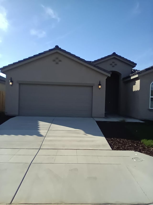 view of front facade featuring a tiled roof, an attached garage, driveway, and stucco siding