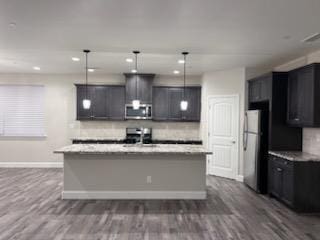 kitchen featuring dark hardwood / wood-style floors, a kitchen island with sink, stainless steel appliances, and decorative light fixtures