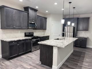 kitchen featuring hardwood / wood-style floors, stainless steel appliances, decorative light fixtures, and a center island with sink