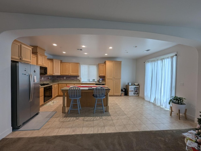 kitchen with light tile patterned floors, light brown cabinets, a breakfast bar area, and black appliances