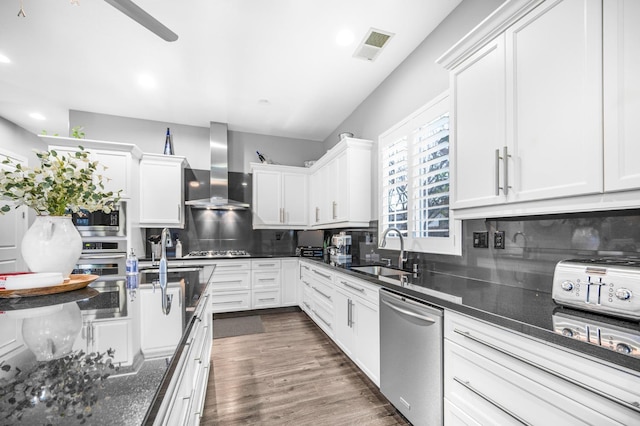 kitchen featuring white cabinets, stainless steel appliances, sink, and wall chimney range hood