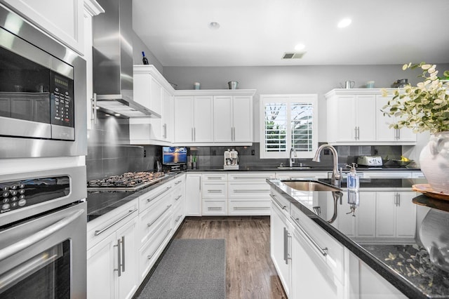 kitchen with stainless steel appliances, white cabinetry, tasteful backsplash, and wall chimney exhaust hood