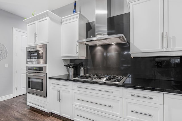 kitchen with appliances with stainless steel finishes, tasteful backsplash, white cabinets, dark hardwood / wood-style flooring, and wall chimney range hood