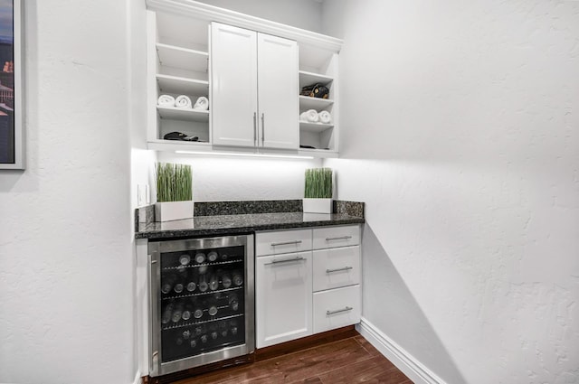 bar with white cabinetry, dark wood-type flooring, beverage cooler, and dark stone counters