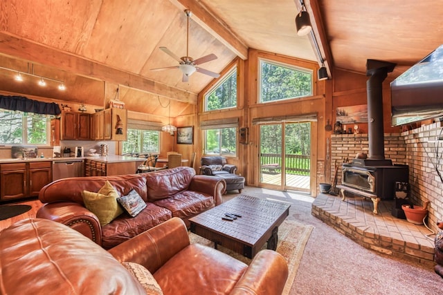 carpeted living room with a wood stove, high vaulted ceiling, ceiling fan with notable chandelier, wooden walls, and beam ceiling