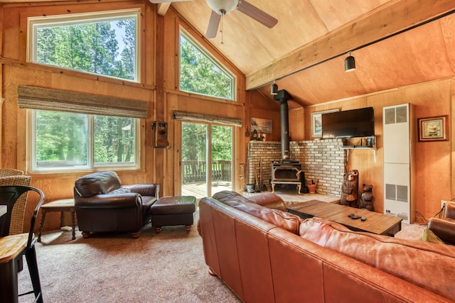 carpeted living room with ceiling fan, wooden ceiling, beamed ceiling, a wood stove, and wood walls