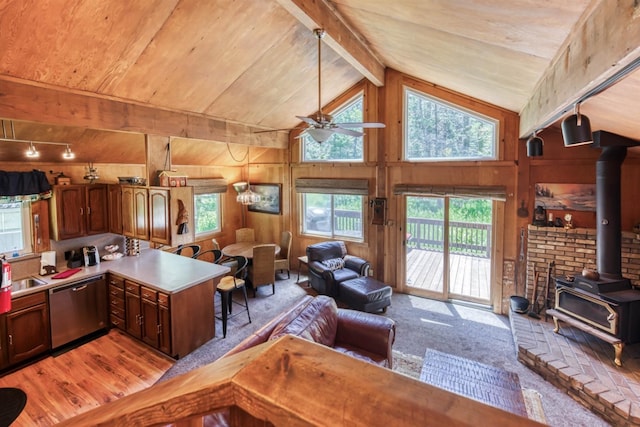 kitchen featuring a wood stove, ceiling fan, beamed ceiling, stainless steel dishwasher, and wood walls