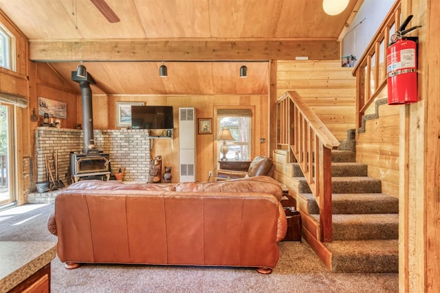 carpeted living room featuring vaulted ceiling with beams, wooden ceiling, a wood stove, and wooden walls