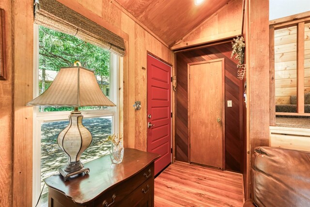 doorway to outside with wooden walls, wood ceiling, lofted ceiling, and light wood-type flooring