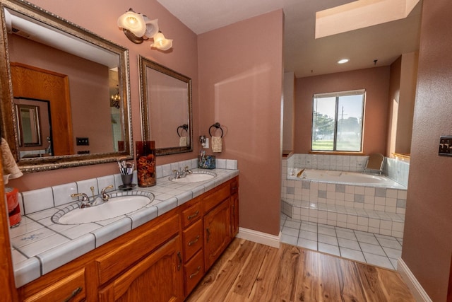 bathroom with a skylight, vanity, hardwood / wood-style floors, and a relaxing tiled tub