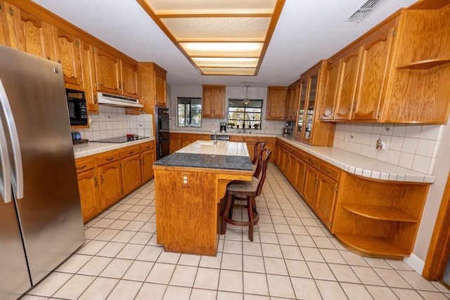 8510 E Nees Ave, Clovis, CA 93619 - kitchen featuring black appliances, open shelves, decorative backsplash, under cabinet range hood, and an island with sink