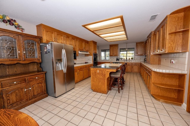 kitchen with a breakfast bar, backsplash, stainless steel refrigerator with ice dispenser, black electric cooktop, and a kitchen island