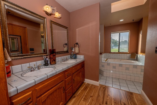 bathroom with hardwood / wood-style floors, vanity, tiled bath, and a skylight