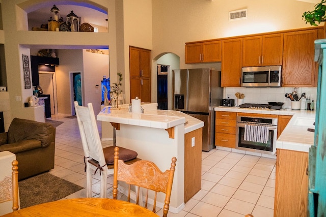 kitchen featuring tile countertops, backsplash, a high ceiling, appliances with stainless steel finishes, and light tile patterned flooring