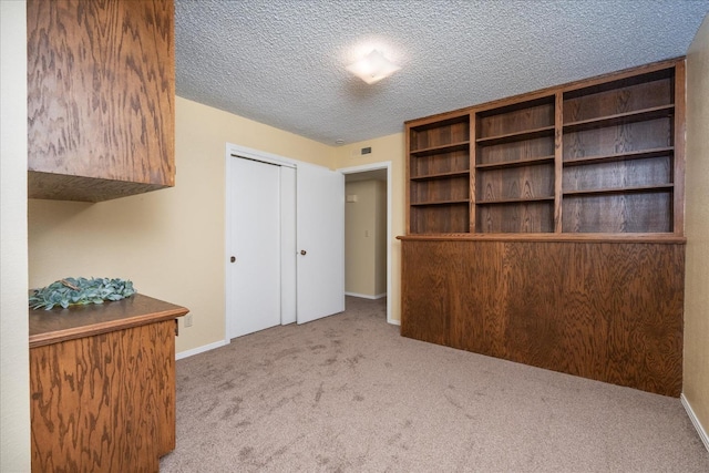 unfurnished bedroom featuring a textured ceiling, carpet floors, visible vents, baseboards, and a closet