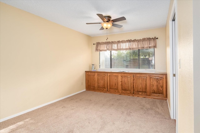 spare room featuring light carpet, ceiling fan, a textured ceiling, and baseboards