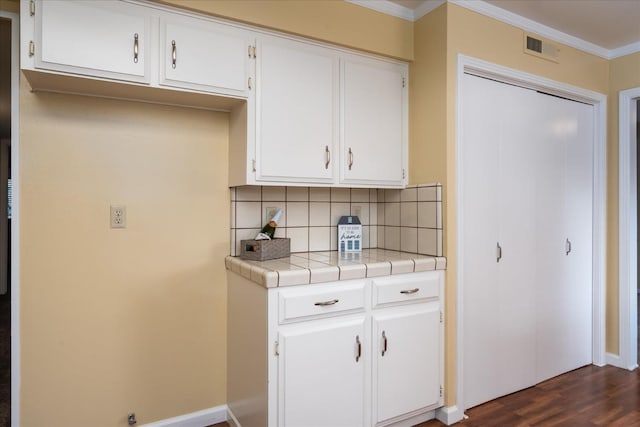 kitchen with dark wood-style floors, crown molding, tile counters, decorative backsplash, and white cabinets