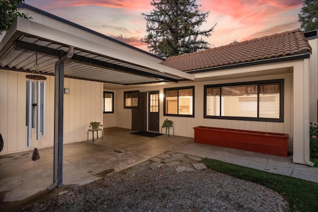 back of house with a tiled roof, an attached carport, and a patio