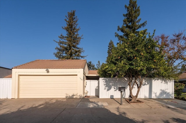 view of front facade featuring fence, a tiled roof, a detached garage, and stucco siding