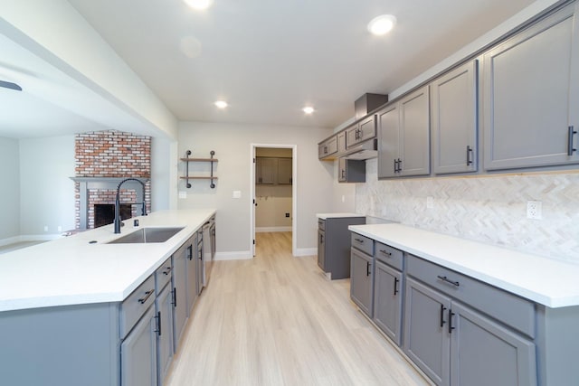 kitchen featuring a brick fireplace, tasteful backsplash, gray cabinets, and a sink