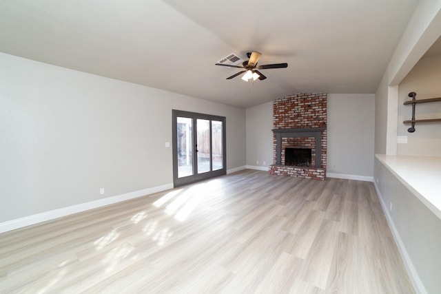 unfurnished living room featuring lofted ceiling, ceiling fan, a brick fireplace, light wood-type flooring, and french doors