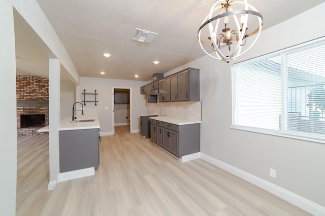 kitchen featuring sink, tasteful backsplash, a chandelier, light hardwood / wood-style flooring, and a fireplace