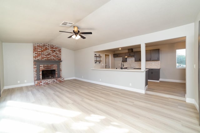 unfurnished living room featuring lofted ceiling, sink, ceiling fan, a brick fireplace, and light wood-type flooring