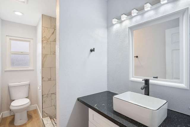 bathroom with a tile shower, toilet, vanity, and hardwood / wood-style flooring