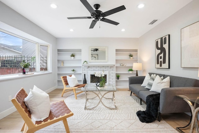 living room with a fireplace, built in shelves, light hardwood / wood-style flooring, and ceiling fan