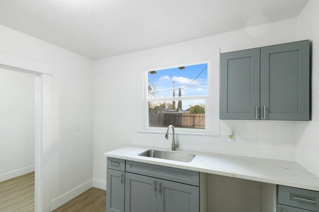 kitchen with sink, dark wood-type flooring, light stone counters, gray cabinets, and decorative backsplash