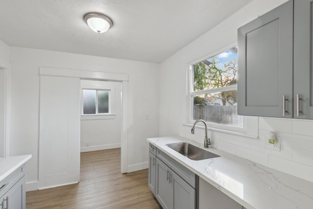 kitchen with gray cabinetry, backsplash, sink, light stone countertops, and light hardwood / wood-style floors