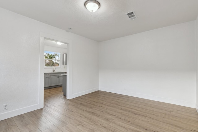 spare room with a textured ceiling, light wood-type flooring, and sink